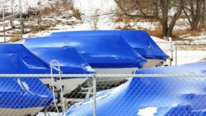 White boats under blue tarp in storage during snowy winter