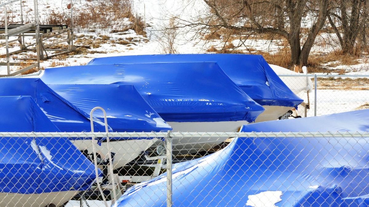 White boats under blue tarp in storage during snowy winter